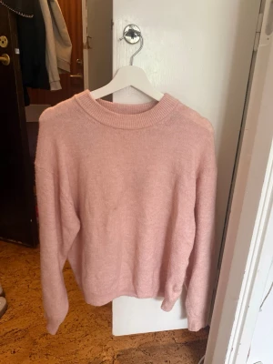 Ljusrosa stickad tröja från H&M - Mysig ljusrosa stickad tröja från H&M med rund halsringning och ribbade muddar. Perfekt för lager-på-lager och enkel att matcha med jeans eller kjol. Tröjan har en avslappnad passform och är superbekväm för kalla dagar.