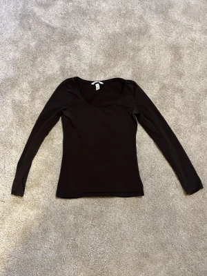 Svart långärmad topp från H&M - En enkel och stilren svart långärmad topp från H&M. Modellen har en rundad halsringning och är figurnära i passformen. Färgen är inte helt svart, den är typ ”off black”, nästan lite mörkbrun eller mörkgrå. Lite urtvättad vid armhålorna men det är inget jag tycker att man märker