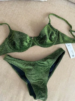 Grön glittrig bikini  - Ny oanvänd bikini från Lindex. Ovadderad, brazilian. Endast provad. Överdelen har kvar prislappen men på underdelen är den borttagen. Överdel - S Underdel - M