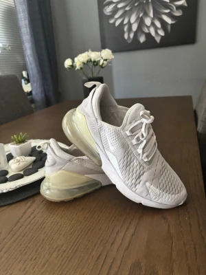 Nike Air Max 270 vita sneakers - Skorna är väl använda men ändå i bra skick. Priset kan diskuteras!   Nike Air Max 270 sneakers i helvitt med mesh-ovandel och stora genomskinliga Air Max-sulor i hälen. Skorna har en sportig design med snörning och diskreta loggor på sidan och plösen. Perfekta för dig som gillar stilrena och bekväma sneakers.