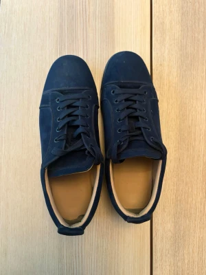 Mörkblå loubs i mocka - Stilrena mörkblå christian Louboutin med ovandel i mocka och matchande mörkblå snörning. Skorna har en låg profil och svart sula. Insidan är ljusbeige och designen är minimalistisk, perfekt för en clean look. Bra skick fraktas snabbt 