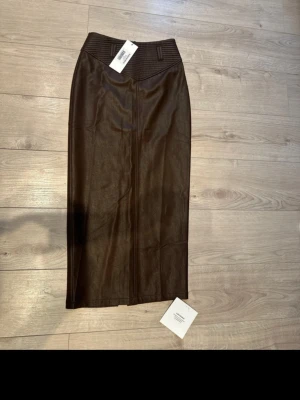 Bristol midi skirt Adoore  - Bristol midi skirt från Adoore  Brun skinnkjol med slits bak.  storlek 36. Dragkedja i midjan   Oanvänd med lappar kvar.