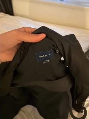 Svart jacka från GANT - Snygg svart jacka från GANT med klassisk design. Jackan har dragkedja och är tillverkad i ett slätt material som känns både stilrent och modernt. Perfekt för dig som vill ha en enkel men trendig jacka till vardags.