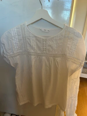 Vit blus med spetsdetaljer - Säljer denna fina blusen från Mango. Har fina detaljer upptill men även vid ärmarna. Säljer då den inte känns som ett plagg för mig längre. Aldrig använd!