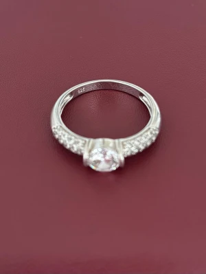 Silverring med gnistrande stenar - Stilren silverring i 925 sterling silver med en stor rund klar sten i mitten och mindre gnistrande stenar längs sidorna. Perfekt för dig som gillar klassiska och eleganta smycken med lite extra bling.