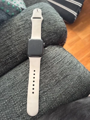 Apple Watch med vit silikonrem - Apple Watch serie 9 40mm med fyrkantig svart skärm och vit silikonrem. Klockan har en stilren design och passar perfekt för dig som vill ha koll på notiser, träning och hälsa direkt på handleden. Remmen är justerbar och mjuk för en bekväm känsla hela dagen.