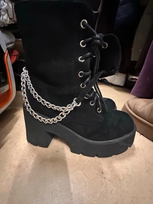 Svarta stövlar med kedja - Snygga svarta stövletter med grov platåklack, snörning framtill och cool silverfärgad kedjedetalj på sidan. Skorna har en robust sula och är tillverkade i mockaliknande material. Perfekta för dig som vill sticka ut med din stil.