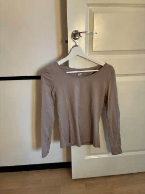 Beige långärmad topp från 157 - En basic beige långärmad topp från 157 med rund halsringning. Tillverkad i mjuk bomull med lite stretch för en skön passform. Perfekt att styla med jeans eller kjol för en enkel och clean look.