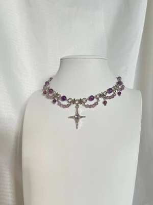 Lila pärlchoker med hänge - Ett halsband med lila och ljuslila pärlor i ametist och i olika storlekar, silverfärgad kedja och ett  stjärnformat hänge i mitten.