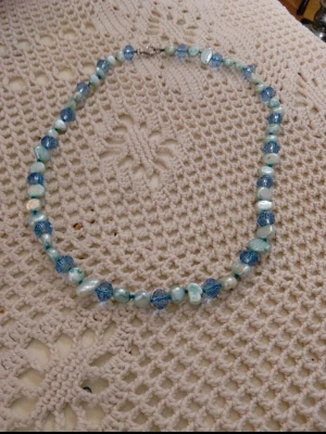 Blått pärlhalsband med mixade pärlor - Snyggt halsband med pärlor i olika nyanser av blått och vitt. Pärlorna är både runda och oregelbundna, vilket ger ett unikt och trendigt uttryck. Perfekt accessoar för att lyfta din outfit med lite färg och stil.