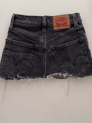 Svart jeanskjol från Levi's - Jag säljer min helt nya, superfina minikjol från Levi’s. Jag köpte den i butik för 400 kr. Kjolen är cirka 33–35 cm lång.Size 23  Jag är 155 cm lång, och på mig täcker den hela rumpan och det blir dessutom kvar ungefär 4–5 cm. Den är alltså ganska kort, men ändå väldigt bekväm att bära och sitter jättefint.  Vid frågor är det bara att skriva till mig i DM. Priset kan diskuteras. Varmt välkommen att höra av dig❤️