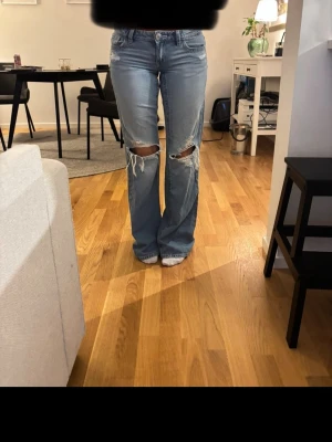 Ljusblå baggy jeans - Säljer ett par ljusblå baggy jeans med stora slitningar och hål på båda knäna. Dom perfekta jeansen! Storleken är XS 14+.