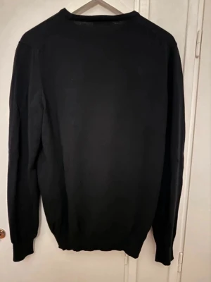 Svart rundhalsad tröja Gran Sasso - Klassisk svart rundhalsad tröja från Gran Sasso, tillverkad i Italien. Tröjan har en enkel och stilren design med ribbade muddar vid ärmslut och nederkant. Perfekt basplagg för en clean look.