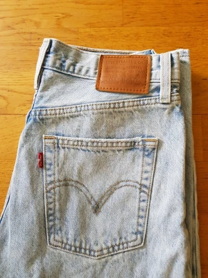 Levi's ljusblåa jeans  - Ljusblå jeans från Levi's med klassisk femficksdesign och ikonisk läderpatch bak i midjan. Jeansen har raka ben och är tillverkade i slitstark denim med tydliga kontrastsömmar och den välkända röda Levi's-taggen på bakfickan.