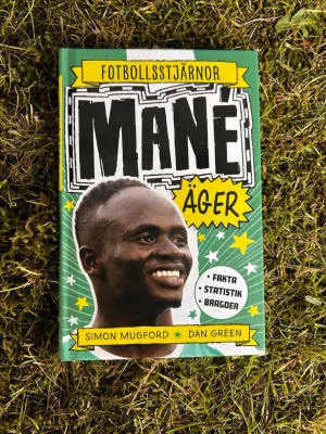 Fotbollsstjärnor: Mané äger - En färgstark bok om fotbollsstjärnan Sadio Mané, skriven av Simon Mugford och Dan Green. Boken har ett grönt och gult omslag med illustrationer, och innehåller fakta, statistik och inspirerande berättelser om Manés resa från Senegal till Liverpool.