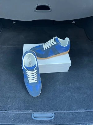 Blå sneakers Maison Margiela - Snygga sneakers från Maison Margiela i blå mocka och läder med vita skosnören och gummisula. Klassisk låg modell med retrovibbar och stilrena detaljer. Perfekta för dig som vill ha något unikt och trendigt i garderoben.
