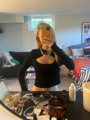 Svart croppad topp med cut-out - Trendig svart croppad topp med lång ärm och snygg cut-out detalj över bröstet. Toppen har en tight passform och är perfekt för att skapa en edgy look. Passar till både jeans och kjol för en cool stil.