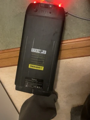 Svart batteripack till elcykel - Säljer ett svart batteripack för elcykel med varningsetiketter och laddningsport. Batteriet har rektangulär form och är tillverkat i plast. Passar till elcyklar och har tydliga anslutningar för laddning och montering.
