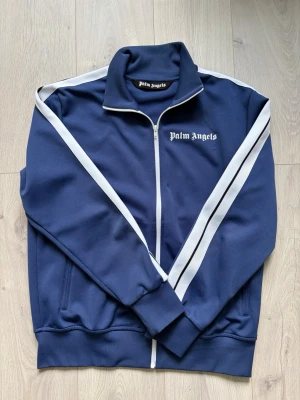 Track jacket - Mörkblå zip tröja från Palm Angels. Ytterst små noppringar under logotyp, inget som påverkar helhetsintryck eller syns vid användning, annars otroligt fräsch. Storlek XL, sitter mer som en M/L. Certilogo finns för att verifiera autenticitet.