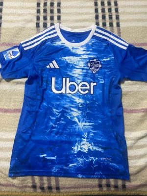 Blå Como 1907 matchtröja Adidas - Säljer en blå matchtröja från Como 1907 med vitt mönster framtill, Adidas-logga och sponsortryck. Tröjan har vita ränder på axlarna, klubbmärke på bröstet och nummer 10 med namnet Nico Paz på ryggen. Tillverkad i funktionsmaterial (AEROREADY). Priset är ej hugget i sten!