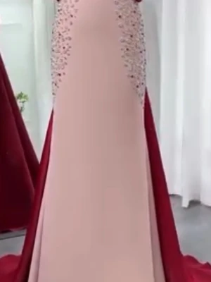Långklänning i rött och beige med paljetter - Elegant långklänning i beige med röda sidor och lång röd släp. Klänningen har paljettdekorationer längs sidorna och en stor rosett baktill. Perfekt för bal eller festliga tillfällen.