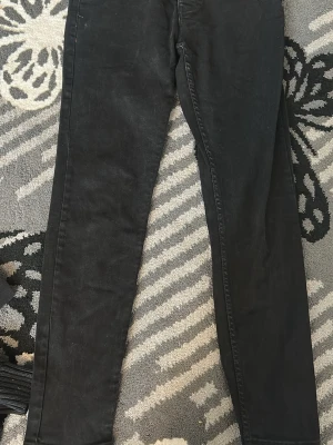 Svarta skinny jeans - Säljer ett par svarta skinny jeans med smal passform och klassisk femficksdesign. Jeansen har normal midja och är tillverkade i stretchigt material för extra komfort. Perfekta till vardagslooken och lätta att matcha med olika stilar.