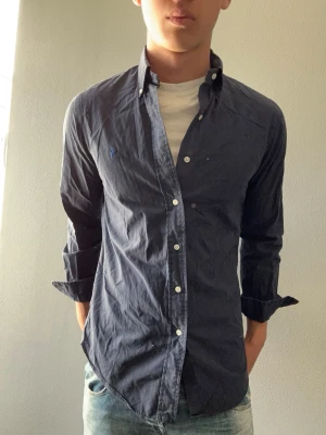 Mörkblå skjorta från Ralph Lauren - Snygg mörkblå skjorta från Ralph Lauren med klassisk krage och knappar framtill. Skjortan har lång ärm och den ikoniska loggan broderad på bröstet. Perfekt till jeans eller chinos för en clean look.
