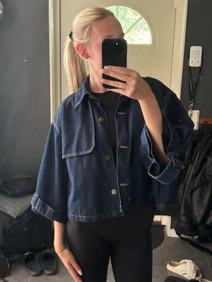 Mörkblå cropped jeansjacka - Snygg mörkblå jeansjacka med oversized passform och vida ärmar. Jackan är cropped och har klassisk krage samt knäppning framtill. Tuffa detaljer med kontrastsömmar och en modern look som passar till många outfits. Tror ej den säljs längre, från Zara. Använd ca 2 gånger 