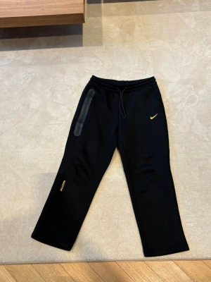 Svarta Nike nocta byxor  - Säljer ett par svarta mjukisbyxor helt oanvända i storlek M från Nike med gul Swoosh-logga och 'NOCTA' tryck på benet. Byxan har en dragkedjeförsedd ficka på sidan. Sköna och stilrena, perfekta för chill eller streetwear. Säljer dessa eftersom jag köpte fel storlek av misstag. Kan gå ner i pris vid snabb affär