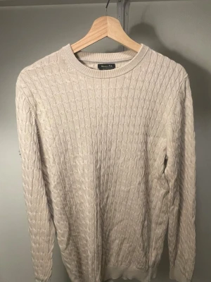 Beige kabelstickad tröja Massimo Dutti - Snygg beige kabelstickad tröja från Massimo Dutti med rund halsringning och ribbade muddar. Tröjan har ett klassiskt mönster och är tillverkad i mjukt bomullsblandning. 