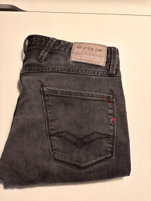 Svarta Replay jeans med röd detalj - Snygga svarta jeans från Replay med klassisk femficksdesign och cool röd broderad detalj på bakfickan. Jeansen har en rak passform och är tillverkade i mjuk bomullsdenim. Perfekta för en trendig och avslappnad stil.