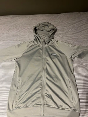 Ljusgrå hoodie från Mckenzie - Snygg ljusgrå hoodie från Mckenzie med dragkedja framtill och två fickor. Hoodien har en klassisk huva och diskret logga på bröstet. Tillverkad i mjukt och stretchigt material som känns skönt mot huden. Perfekt för en avslappnad och stilren look.