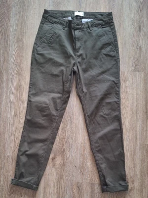 Olivgröna chinos med uppvik - Snygga olivgröna chinos med smal passform och uppvikta benslut. Byxorna har snedställda fickor fram och två bakfickor med knapp. 