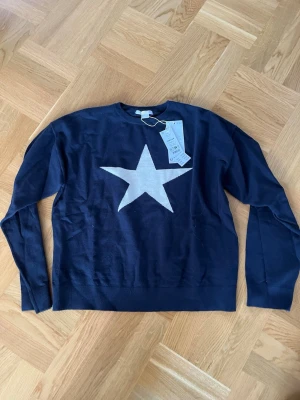 Mörkblå stickad tröja med stjärna från Gina Tricot - Ny mörkblå stickad tröja från Gina Tricot  med en stor vit stjärna på bröstet. Tröjan har rund halsringning och långa ärmar, perfekt för dig som gillar enkel men cool design. 