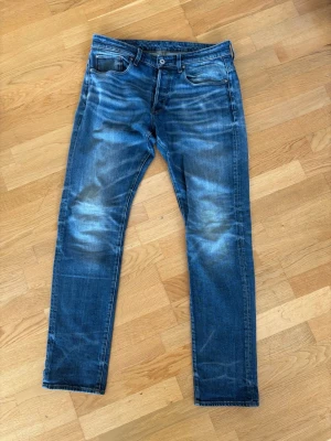 Blå jeans från G-Star RAW - Snygga blå jeans från G-Star RAW med klassisk femficksmodell och slitna detaljer. Jeansen har en rak passform och är gjorda i denim med coola tvättade effekter. Perfekta för en avslappnad och trendig stil.