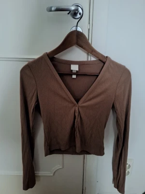 Brun tröja - Snygg brun tröja med v-ringning och långa ärmar. Toppen har knappar framtill för en extra detalj. Perfekt att styla med lågmidgade jeans eller shorts. 