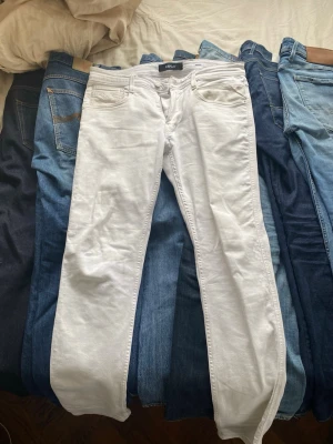 Vita Replay jeans - Snygga vita slim fit jeans från Replay med klassisk femficksmodell och dragkedjegylf. Jeansen har raka ben och är tillverkade i ett mjukt bomullsmaterial med stretch för extra komfort. Perfekta för en clean och fräsch look. Modell: Anbass. 