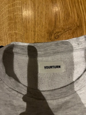 Ljusgrå hoodie från YOURTURN - En stilren ljusgrå hoodie från YOURTURN i mjukt bomullsmaterial. Klassisk modell med ribbade muddar vid ärmslut och midja. Perfekt för en avslappnad och enkel look.