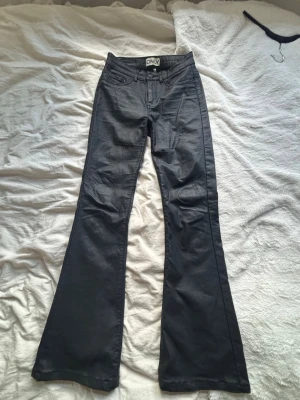 Svarta bootcut-skinnbyxor från ONLY - Snygga svarta bootcut-skinnbyxor från ONLY med klassisk femficksdesign och utsvängda ben. Byxorna har normal midja och är tillverkade i ett stretchigt material som ger en bekväm passform. Byxorna är 30 i längd. 