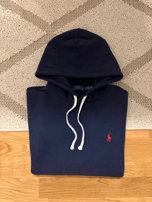 Mörkblå Polo Ralph Lauren Hoodie - Hej!👋   Säljer en mörkblå Polo Ralph Lauren Fleece Hoodie. Hoodien är i mycket gott skick och har inga fläckar eller hål. Den har använts ett antal gånger och köptes second hand för ca 1 år sedan. Storlek: M i herr, 175/96A Mått skickas privat😀  Skickar snabbt!🚛📦  Hör av er vid frågor💯