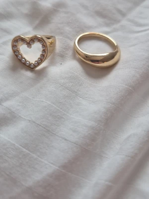 Två guldfärgade ringar, en med pärlor - Två fina guldiga ringar, båda köpta från glitter, aldrig använt då de båda är för stora. Kostar 200-300 kr sammanlagt men mitt pris är 85!