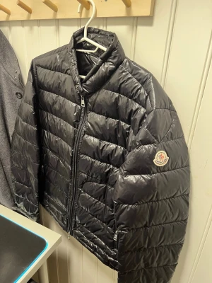 Svart dunjacka moncler Acorus size 2 cond 9/10 - Snygg svart dunjacka från Moncler med glansig finish och klassisk quiltad design. Jackan har hög krage, två dragkedjeförsedda fickor och Moncler-logga på ärmen. Perfekt för våren! Riktigt snygg ser helt ny ut. Såklart äkta! 