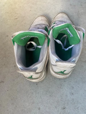 Vita och gröna Air Jordan 4 sneakers - Snygga Air Jordan 4 sneakers i vitt med gröna detaljer och klassisk Jumpman-logga på plös och häl. Skorna har meshpaneler, gröna accenter och vita skosnören. Perfekta för dig som gillar streetwear och vill sticka ut med en ikonisk modell.