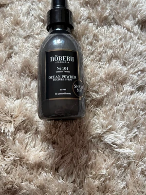 Nõberu Ocean Powder Texture Spray - Ocean Powder Texture Spray från Nõberu Stockholm, doft Tobacco Vanilla, No 104. Flaskan är svart med guld- och vit text, rymmer 150 ml och har sprayfunktion. Perfekt för att skapa textur och volym i håret. Snygg och stilren design.