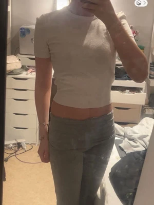 Ljusbeige croppad topp från H&M - En enkel och stilren ljusbeige croppad topp från H&M. Toppen har korta ärmar, rund halsringning och är tillverkad i ett mjukt bomullsmaterial. Perfekt för en avslappnad och trendig look.