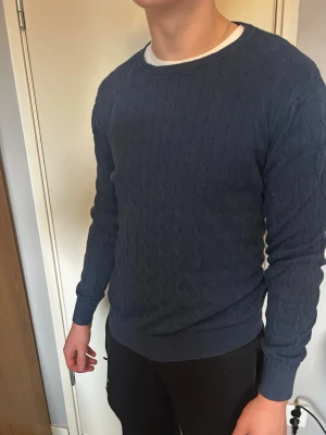 Kabelstickad tröja från dressman - Mörkblå kabelstickad tröja från dressman  med rund halsringning och ribbade muddar vid ärmslut och nederkant. Tröjan har ett klassiskt mönster och är perfekt för lager-på-lager. Passar till många olika stilar. Passar även en storlek L. Modellen på bilden är 184cm och väger 85kg. Priset kan diskuteras😁🙌