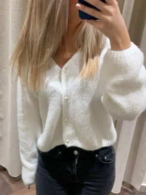 Vit stickad kofta med pärlknappar - Mysig vit stickad kofta med v-ringning och dekorativa pärlknappar framtill. Koftan har ballongärmar och ribbade muddar vid ärmslut och nederkant. 💞💞
