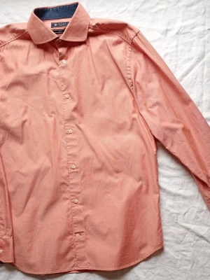 Ljusrosa skjorta från Riley - Snygg ljusrosa skjorta från Riley med klassisk krage och knappar framtill. Skjortan har lång ärm och är tillverkad i mjuk bomull, perfekt för en clean och stilren look.