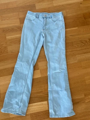Ljusblå bootcut jeans - Säljer ett par ljusblå bootcut jeans med klassisk femficksdesign och bälteshällor. Jeansen har en snygg utsvängd passform och är perfekta för en avslappnad och trendig look. Materialet är mjukt denim i bomull.