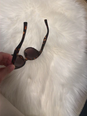 Bruna solglasögon med leopardmönster - Snygga solglasögon med rundade bågar i brun leopardmönstrad plast. Glasen är mörka och ger en cool retrovibe. Perfekta för soliga dagar när du vill sticka ut lite extra.